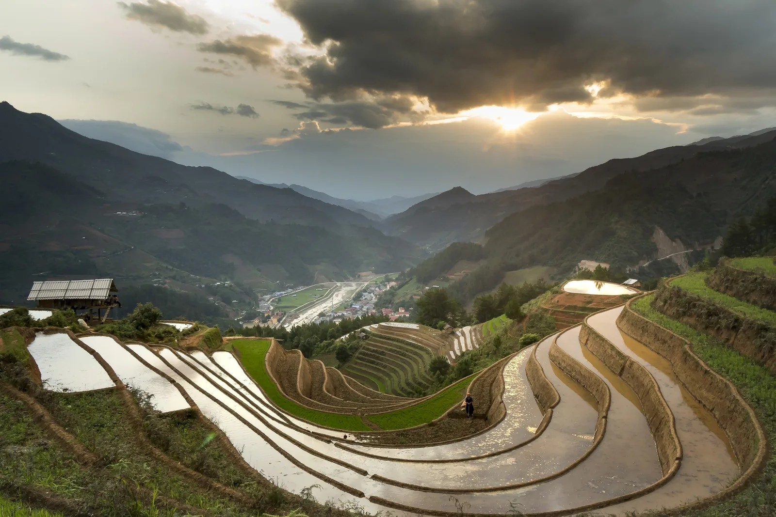 Water-filled terraced rice paddies curve through a mountain valley at sunset in Ha Giang, Vietnam.