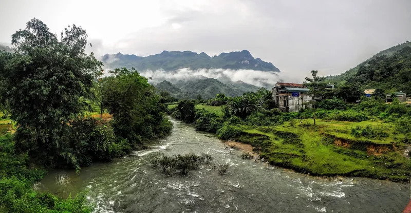 A river winds through green fields toward misty mountains near Minh Tan, Ha Giang province.