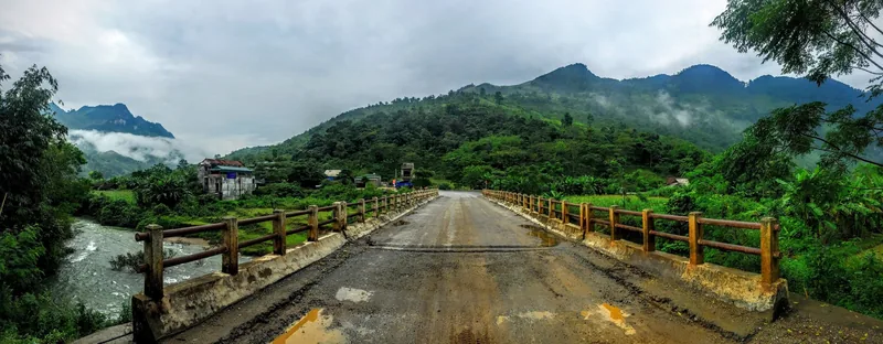 A concrete bridge crosses a river toward misty green mountains near Minh Tan, Ha Giang province.
