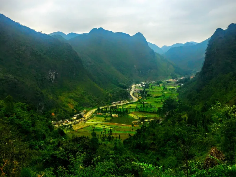 A winding road and river cut through a lush green valley surrounded by limestone mountains in Ha Giang.