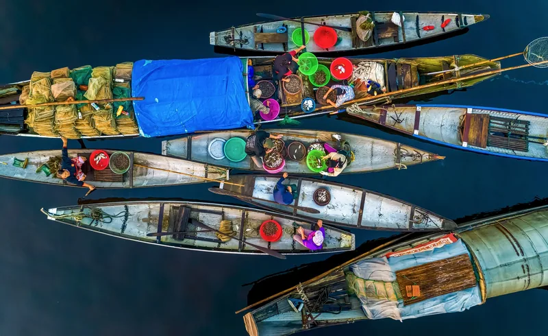 Aerial view of narrow wooden boats loaded with colorful baskets and nets on Tam Giang lagoon.