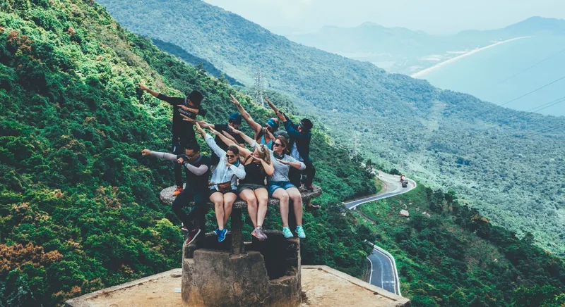 Travelers pose playfully atop a stone marker overlooking the winding Hai Van Pass and coastline near Hue.