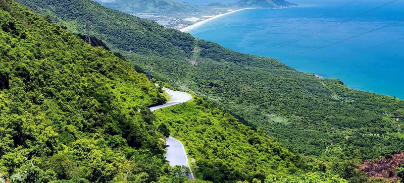 A winding road cuts through green mountains overlooking the coastline at Hai Van Pass near Hue.