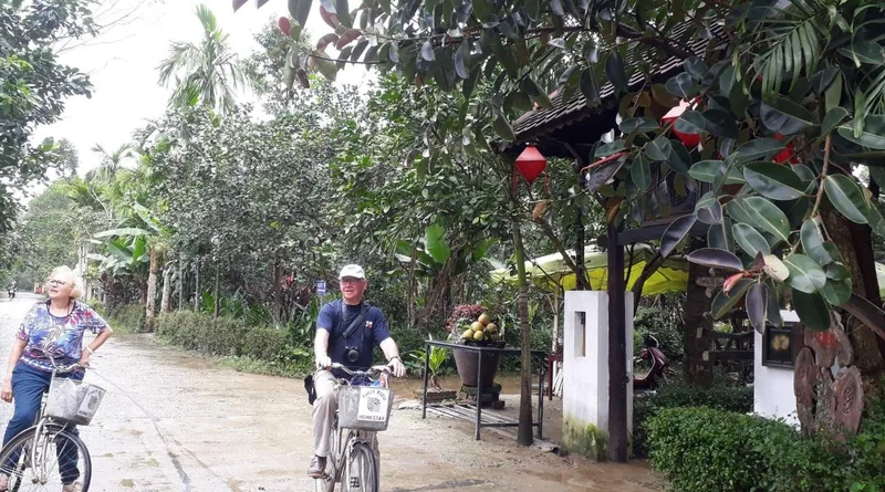 Tourists cycle along a shaded lane past lush gardens and red lanterns in Thuy Bieu village near Hue.