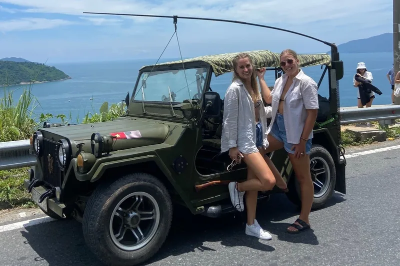 Two women pose beside a military-style jeep overlooking the coastal bay road near Hue.
