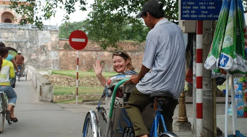 A smiling tourist waves while riding a cyclo through Hue's old citadel streets in Vietnam.