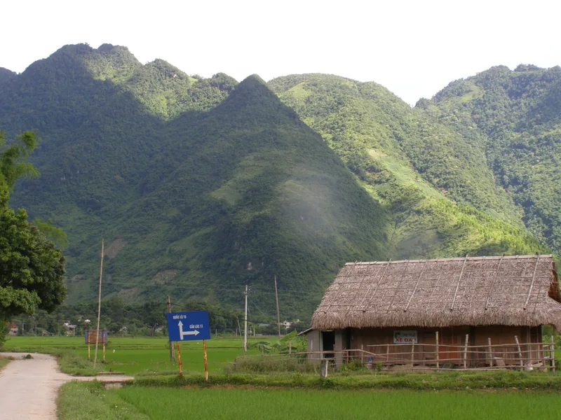 A thatched-roof stilt house sits beside rice paddies below jagged green mountains in Mai Chau valley. A thatched-roof stilt house sits beside rice paddies below jagged green mountains in Mai Chau valley.