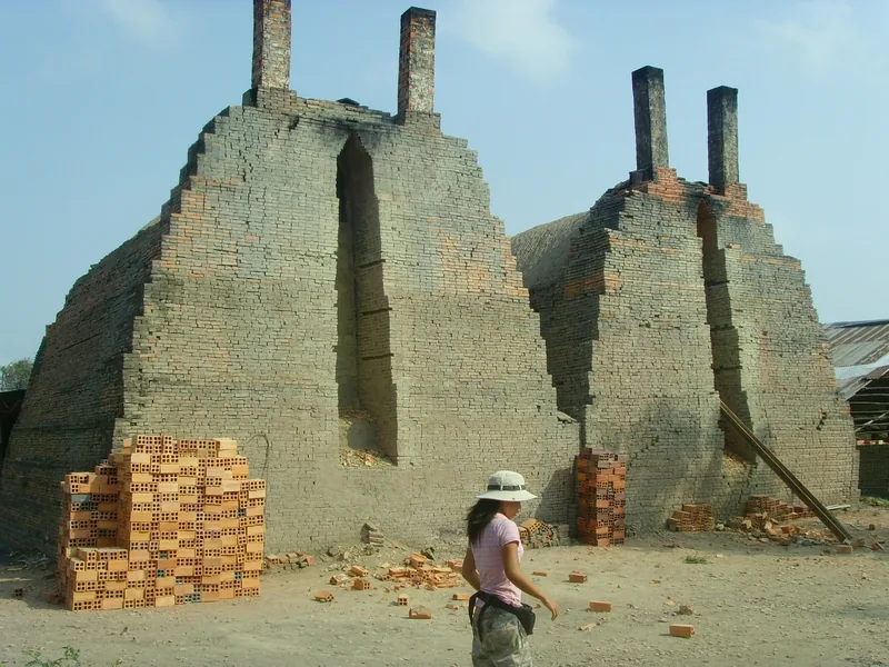 Traditional beehive brick kilns with tall chimneys and stacked bricks at a factory in the Mekong Delta, Vietnam.